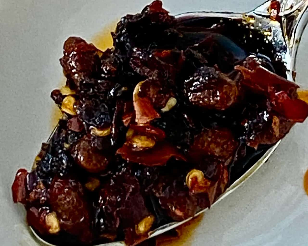 Spoonful of chili crisp showing fried chile pieces, seeds, and oil